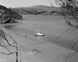 The boat ‘Fathom’ and its two passengers are blown into Rāpaki beach whilst trying to reach Ōhinehou. Small rock pools like the one in the foreground are often seen on the beach at low tide. If you dig deep enough in the sand hot springs can be found, reminding the community that Whakaraupō is the inner rim of a dormant volcano.
